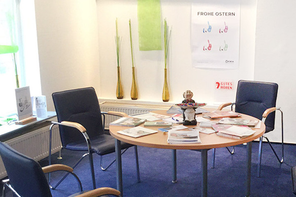 Heller Wartebereich mit Stühlen, Tisch voller Broschüren und Osterdekoration in einem Hörakustik-Fachgeschäft.